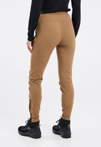 Bruine actieve broeken met een aansluitend ontwerp, rekbaar materiaal en ritsen bij de enkels. Gecombineerd met zwarte wandelschoenen.