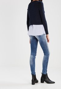 Navy-Strickpullover über einem hellblauen gestreiften Hemd, kombiniert mit ausgewaschenen blauen Skinny Jeans und schwarzen Stiefeletten.