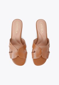 Brązowe skórzane klapki z krzywymi paskami, subtelnymi detalami przeszycia i małym metalowym akcentem. Gładka matowa tekstura i otwarty czubek.