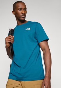 Teal kortærmet t-shirt lavet af bomuld med rund hals. Har et hvidt logo på venstre bryst og en glat tekstur.