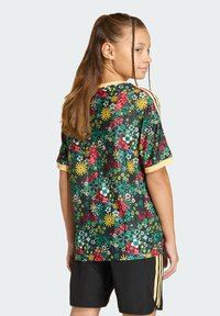 Κοντομάνικη φλοράλ φανέλα σε μαύρο χρώμα με ζωντανά πολύχρωμα λουλούδια, κίτρινα στοιχεία και άνετη γραμμή, συνδυασμένη με μαύρο σορτς με ρίγες.