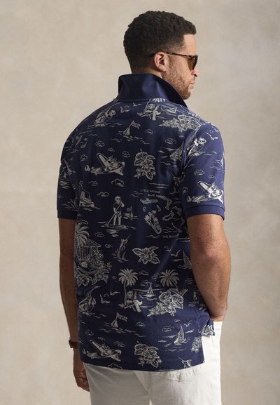 Μπλουζάκι πόλο σε ναυτικό μπλε με κοντά μανίκια, διακοσμημένο με λευκές αυθεντικές θαλασσινές  εικόνες, γιακά που διπλώνει προς τα κάτω και ευθεία τελείωμα, κατασκευασμένο από υφή υφάσματος.