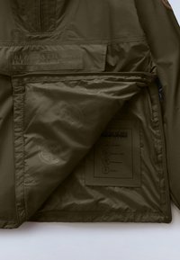 Λαδί πράσινο μπουφάν με υφή εξωτερικής επιφάνειας, που διαθέτει εμπρόσθια τσέπη με φερμουάρ, εσωτερικές ετικέτες και σχεδίαση γιακά με ημιδιακοπή φερμουάρ. Αδιάβροχο υλικό.