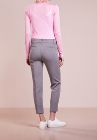 Lichtroze longsleeve top met een V-hals. Grijze tapered pantalon met een getailleerde pasvorm. Witte sneakers maken de outfit af. Gladde structuur door het geheel.