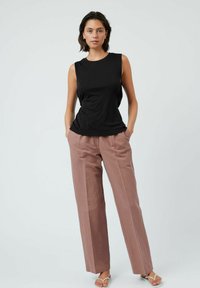 Top nero senza maniche con scollo rotondo abbinato a pantaloni a palazzo a vita alta rosa chiaro e sandali piatti bianchi.