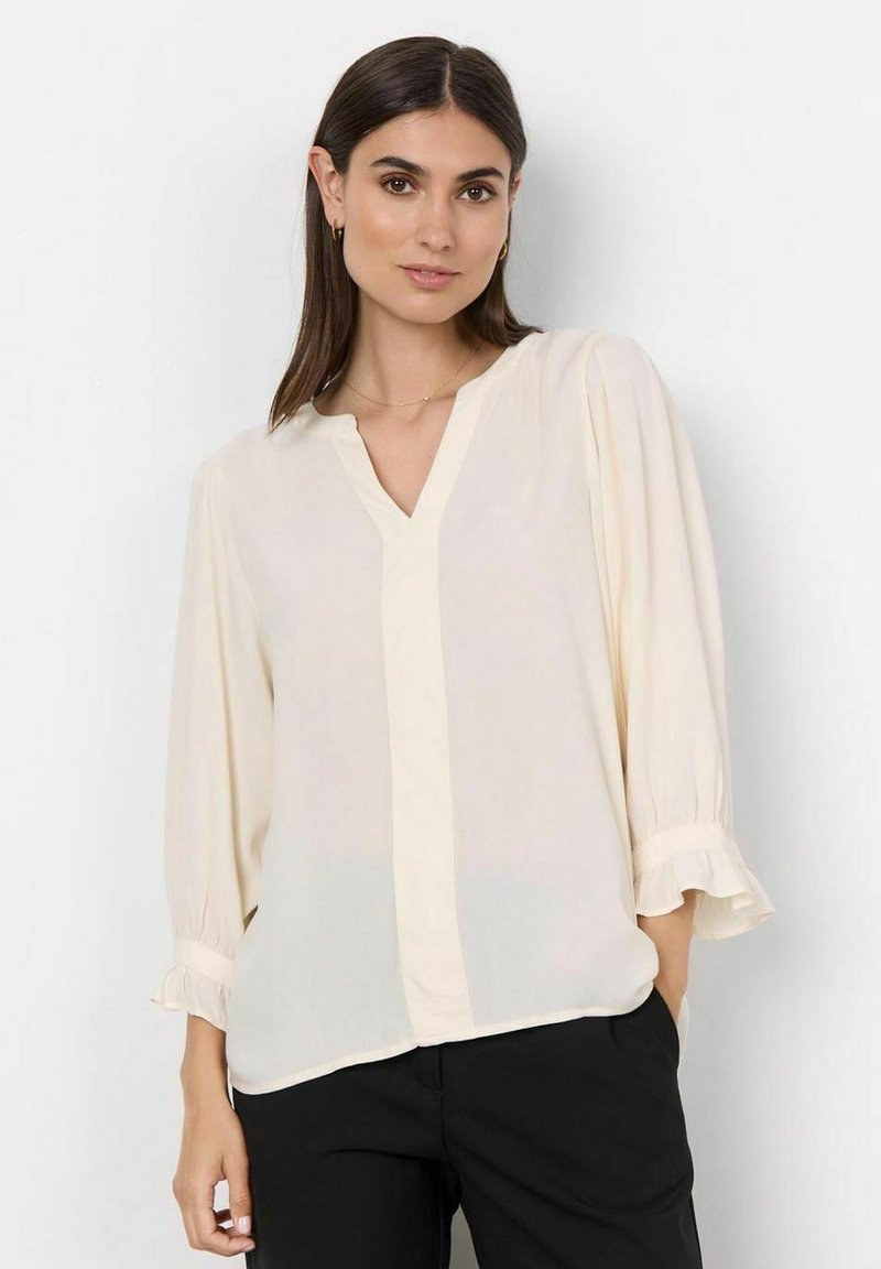 Helle Cremefarbene Bluse aus transparenter Stoff, mit V-Ausschnitt, Dreiviertelärmeln mit Rüschensaum und einem schmalen vertikalen Vorderteil.
