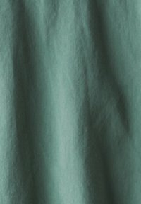 Tissu texturé dans une teinte de vert discret, affichant des variations subtiles et des ombres, indiquant douceur et fluidité. Aucun motif ou élément métallique visible.