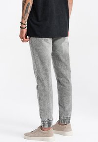 Pantalons de jogging gris clair avec une taille et des poignets élastiques, fabriqués dans un matériau semblable à du denim, associés à des baskets beiges. Texturés avec un aspect délavé.