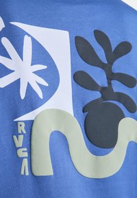 Tessuto blu con forme astratte tra cui una stella bianca a raggi, una pianta nera arrotondata, una linea ondulata beige e le lettere RVCA in beige.