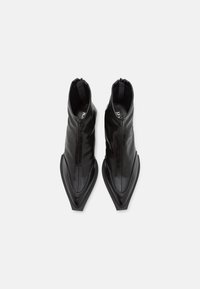 Bottes basses en cuir noir avec une texture lisse, design à bout pointu et fermeture éclair à l'arrière. Dispose d'une semelle plate et structurée pour la stabilité.