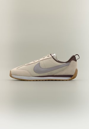 Beżowo-brązowy sneaker Nike z szarym logo, gumową podeszwą i sznurowanym designem, pokazany z boku na neutralnym tle.