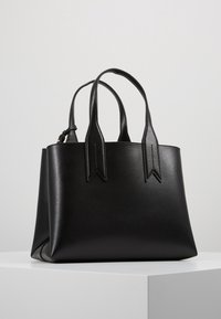 Svart läderhandväska med rundade kanter och dubbla handtag. Har en texturerad yta och spetsiga detaljer på handtagen.