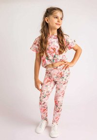 Zestaw odzieżowy w kwiaty składający się z różowej bluzki z krótkim rękawem oraz dopasowanych legginsów w kwiatowy nadruk, wykonany z elastycznego materiału, zestawiony z białymi sneakersami.