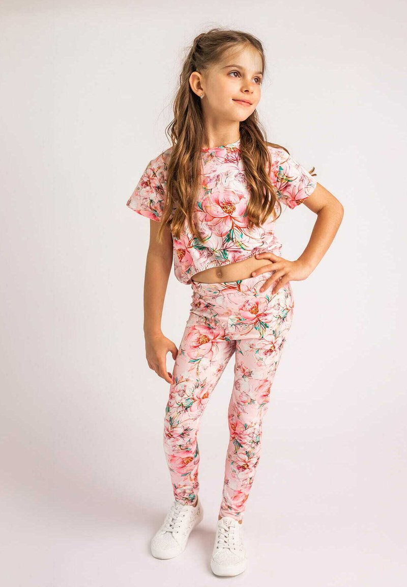 Zestaw odzieżowy w kwiaty składający się z różowej bluzki z krótkim rękawem oraz dopasowanych legginsów w kwiatowy nadruk, wykonany z elastycznego materiału, zestawiony z białymi sneakersami.