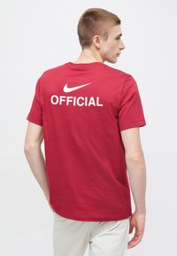 Červené bavlnené tričko s logom "NIKE" a bielym nápisom "OFFICIAL" na chrbte. Štandardný strih s krátkymi rukávmi a okrúhlym výstrihom.