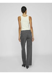 Šedé kalhoty s širokými nohavicemi a vysokým pasem, které jsou kombinovány s světlým, upnutým topem. Obsahují dvě zadní kapsy a lem těsně nad botami.