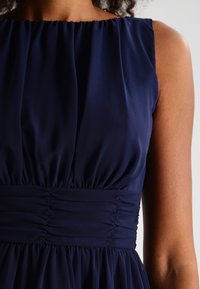 Robe bleu marine avec un corsage froncé, texture unie et ruché élastique à la taille, avec des manches larges et une jupe fluide.