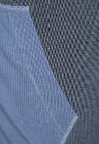 Tela texturizada que muestra secciones en gris oscuro y azul claro con costuras distintivas. Las formas crean un diseño moderno y en capas.