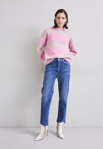 Maglione a maglia oversize in gradient rosa e beige, abbinato a jeans blu a gamba dritta e stivali alla caviglia bianchi in pelle di serpente con punta affusolata.