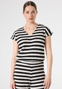 Top a rayas en blanco y negro con escote en V y mangas cortas. Tejido texturizado con un patrón ondulado, pieza inferior a juego visible.