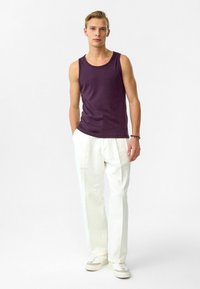 Paarse tanktop, witte op maat gemaakte broek en beige sneakers. De top heeft een ronde halslijn; de broek heeft een geplooid ontwerp.