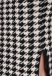 Zwart-wit gekleurde houndstooth gebreide stof met een zijopening, met een zachte textuur en gestructureerd ontwerp.