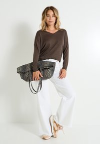 Top metálico marrón de manga larga, jeans blancos de pierna ancha, zapatillas beige con detalles. Bolso de estampado de leopardo con dos asas y cierre plegable.