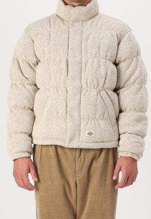 Puffjacka i beige, tillverkad av strukturerad tyg. Har en hög krage, elastiska mudd, och två sidofickor. Bärs över manchesterbyxor.