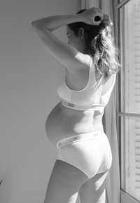 Weißes Umstandsunterwäsche-Set mit nahtloser Bralette und niedrig geschnittenen Slips. Der Stoff wirkt weich und dehnbar, um einen wachsenden Bauch aufzunehmen.