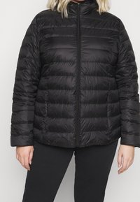 Giacca imbottita nera con collo alto, caratterizzata da sezioni trapuntate orizzontali, chiusura frontale con cerniera e tasche laterali. Finitura liscia e leggera.