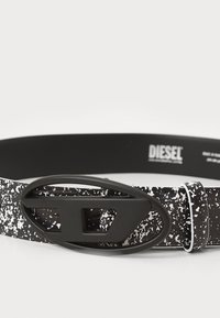 Ceinture à motif noir et blanc fabriquée dans un matériau durable, dotée d'une grande boucle ovale noire et d'une finition lisse avec une texture minimale.