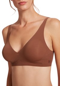 Top in microfibra marrone, senza cuciture, con scollatura a V profonda e sottili spalline. Texture liscia con hardware ridotto al minimo. Nessuna imbottitura visibile.