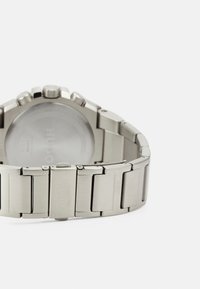 Uhr aus Edelstahl mit einem gebürsteten Metallarmband, rundem Zifferblatt und Multifunktions-Chronographenknöpfen. Logo auf der Schließe eingraviert.