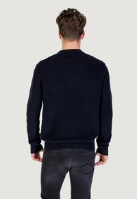 Maglione a coste blu navy con scollatura tonda e maniche lunghe, caratterizzato da un tessuto testurizzato e una vestibilità comoda. Abbinato a jeans grigio scuro.