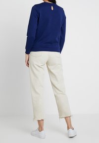 Tummansininen collegepaita, jonka selkäpuolella on aukko, yhdistettynä maanläheisiin lyhyisiin farkkulaskeutumiin, joissa on repsottavat helmukset, ja valkoisiin sneaker-kenkiin.