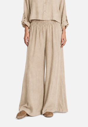Pantaloni beige a gamba larga con vita elasticizzata abbinati a una camicia morbida abbottonata coordinata e scarpe slip-on intrecciate marroni.