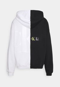 Felpa con cappuccio divisa verticalmente in bianco e nero. Presenta un grande logo "CK" bianco a sinistra e un logo "CK" multicolore più piccolo a destra.