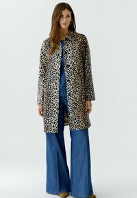 Leopardenmuster-Mantel mit einem Kragen, langen Ärmeln und geradem Schnitt. Kombiniert mit ausgestellten Jeanshosen und gelben Schuhen.