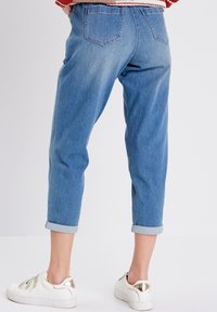 Jean en denim bleu clair avec des ourlets retroussés, design à cinq poches et une coupe légèrement ample, associés à des baskets blanches avec des accents dorés.