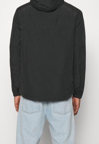 Svart huva jacka med en texturerad yta, elastiska mudd, och en rak kant, kombinerad med ljusblå denimjeans.