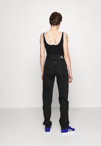 Jeans negros de cintura alta con pierna recta, combinados con una camiseta sin mangas negra con tirantes blancos y espalda descubierta. Zapatillas deportivas azules completan el look.