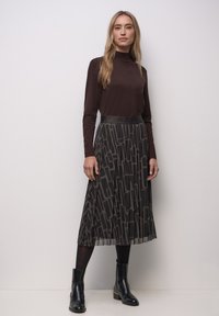 Bruine coltrui gecombineerd met een geplooide zwarte rok met een geometrisch patroon, aangevuld met zwarte enkellaarsjes.
