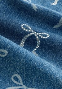 Denim-kangas, jossa on sininen sävy, valkoisia nauhakuvioita ja kirkaita strasseja, luoden tekstuurimaisen ja heijastavan pinnan.
