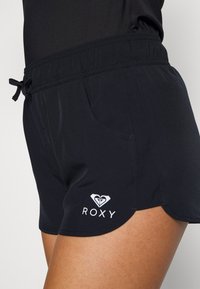 Čierne plavky s elastickým pásom a šnúrkou, s bočnými vreckami a okrajom vlniek. Biele logo Roxy na prednej strane.