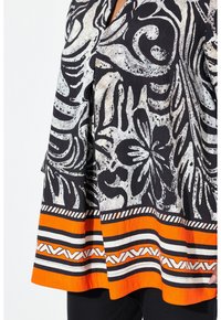 Zwarte top met witte bloemmotieven en een oranje gestreepte zoom. Lichtgewicht stof met een relaxte pasvorm en opvallende patronen aan de onderkant.