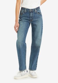 Light blue denim straight-leg jeans with a mid-rise waist, five pockets, and contrasting stitching. Hem slightly frayed, worn with white sneakers.