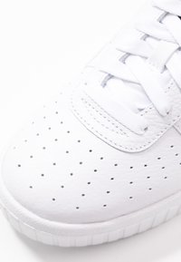 Baskets blanches avec une tige en cuir à détails perforés, lacets plats et semelle en caoutchouc texturée. Accents gris clair.