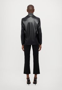 Svart kavaj i faux läder med en skräddarsydd passform, en strukturerad krage och långa ärmar. Bärs över figursydda svarta utsvängda byxor och svarta klackar.