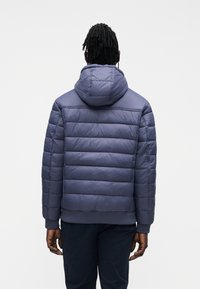 Navy blue puffer jacket with a hood, featuring horizontal quilted sections, elastic cuffs, and a ribbed waistband. Smooth texture.