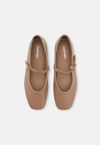 Brown faux leather Mary Jane shoes with an adjustable strap, rounded toe, and smooth texture. Features subtle brand logo on the insole.